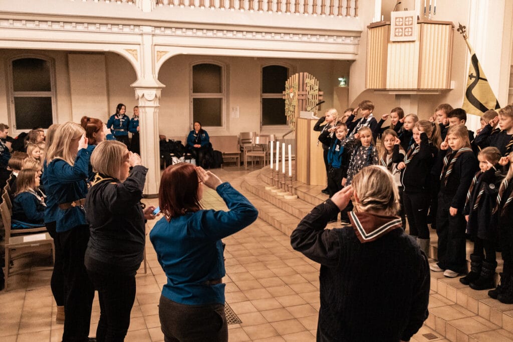 Sudenpennut antamassa partiolupaustaan tehden partiotervehdyksen. Johtajat seisovat edessä ja ottavat lupauksen vastaan.