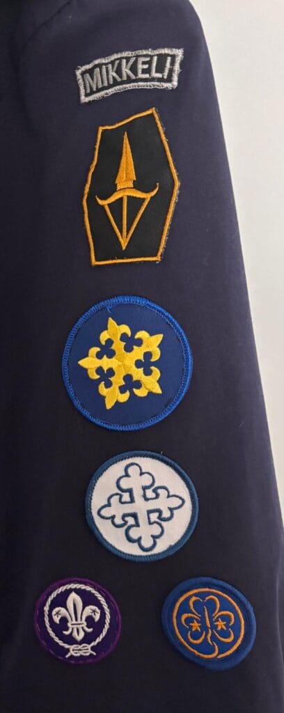 Partiopaidan vasen hiha. Hihassa ylhäällä alaspäin katsottuna paikkakuntatunnus, piiritunnus, keskusjärjestötunnus ja maailmanjärjestöjen (WOSM, WAGGGS) tunnukset.